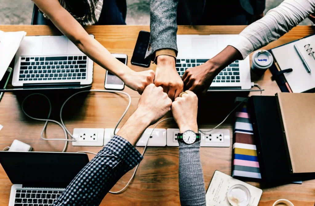 Benefits of Human and AI, image depicting five human hands fist bumping.